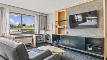 A modern hotel room with a large bed, a flat-screen TV mounted on a stone wall, a desk with a chair, and a sofa.