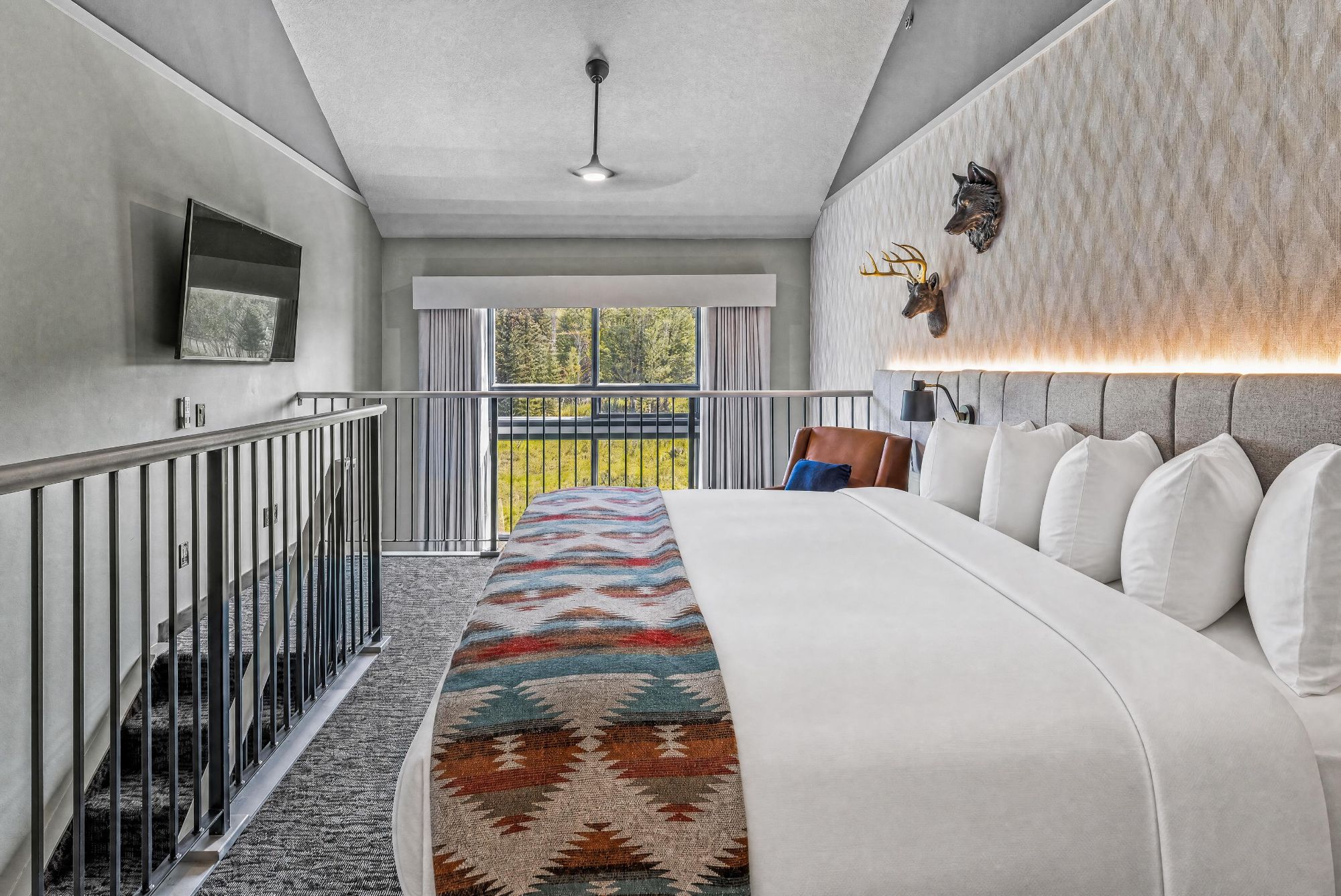 A modern hotel room with a large bed, a view of the outdoors, a balcony, and a mounted animal head decoration.
