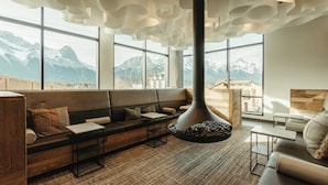 Un intérieur moderne avec un canapé, des tables et une cheminée. De grandes fenêtres offrent une vue sur les montagnes.