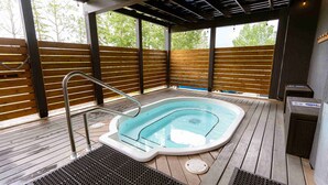 Un bain à remous sur une terrasse en bois, avec un escalier en métal, entouré de lattes de bois et d’une rambarde en métal.