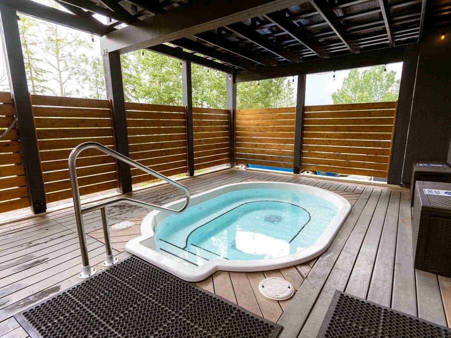 A hot tub on a wooden deck with a metal ladder, surrounded by wooden slats and a metal railing.