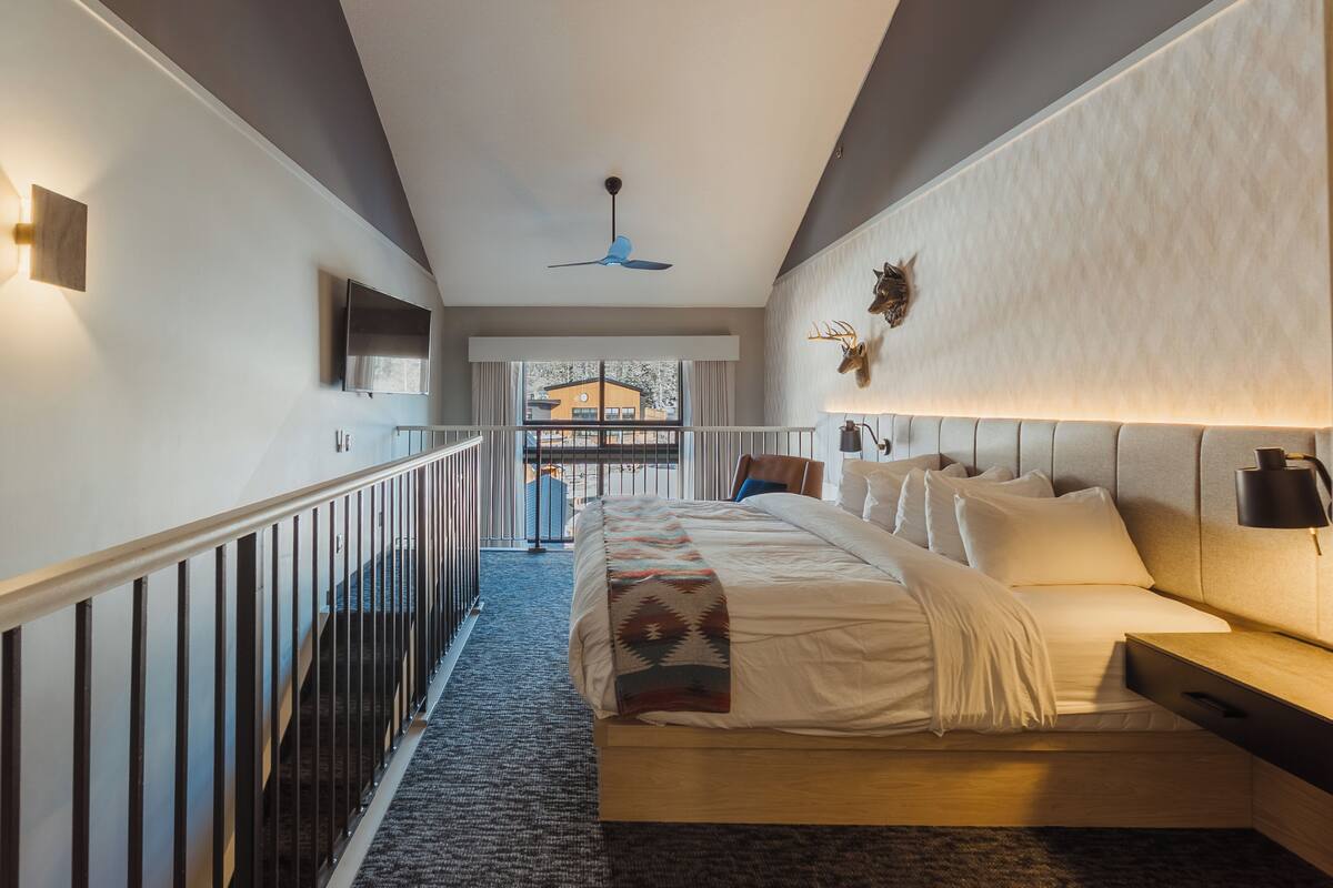 Une chambre à coucher avec un lit, des tables de chevet, un ventilateur de plafond et une vue sur l’extérieur.