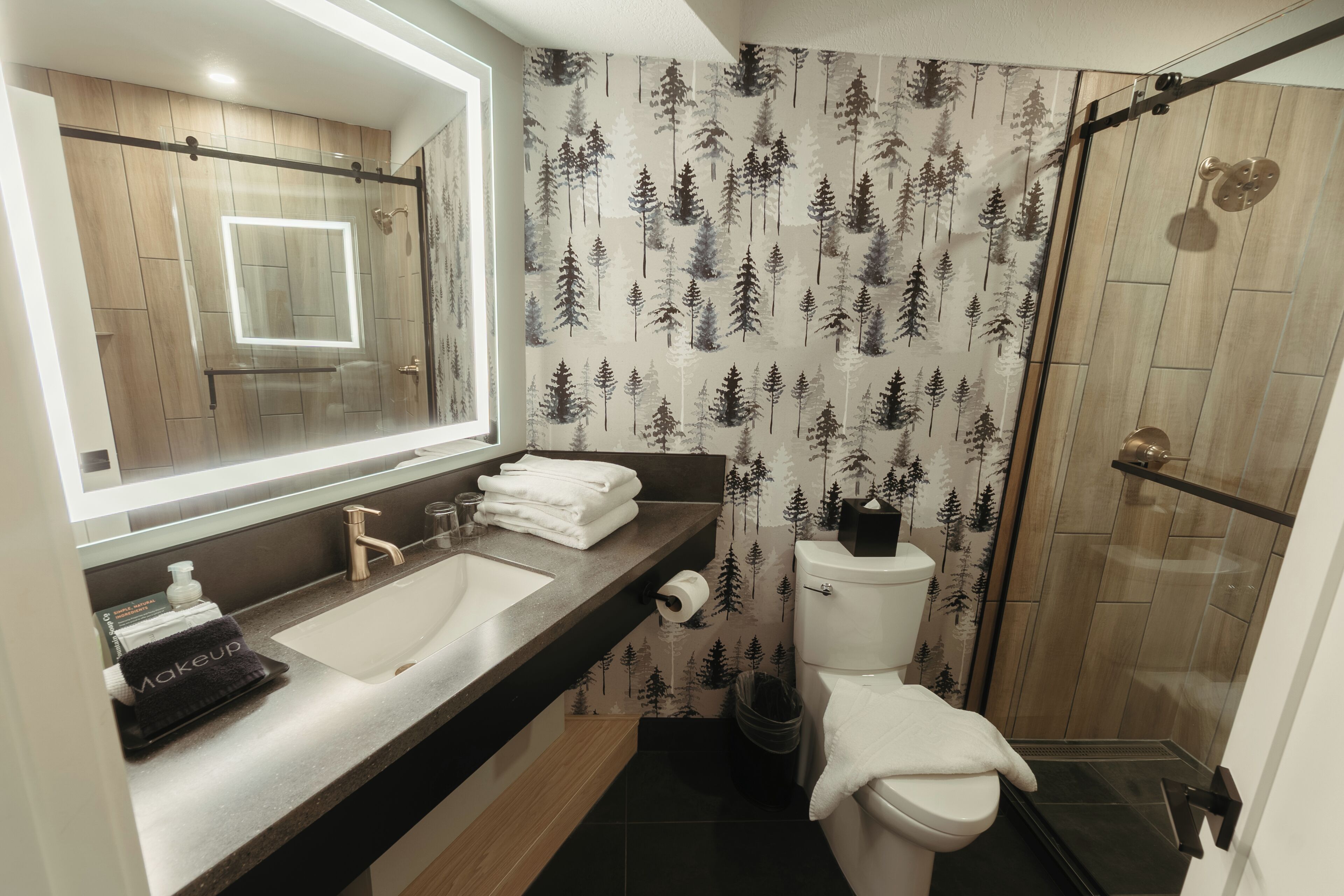 A modern bathroom with a large mirror, dual sinks, a toilet, and a shower area.