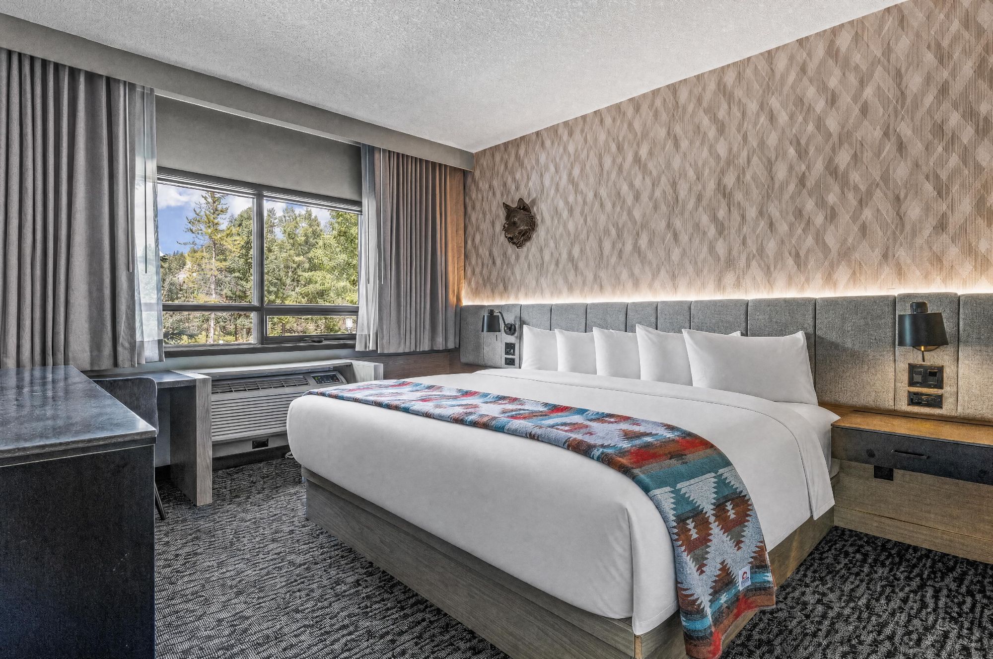 Une chambre d’hôtel avec un grand lit, un bureau, une fenêtre et un mur décoré de motifs.