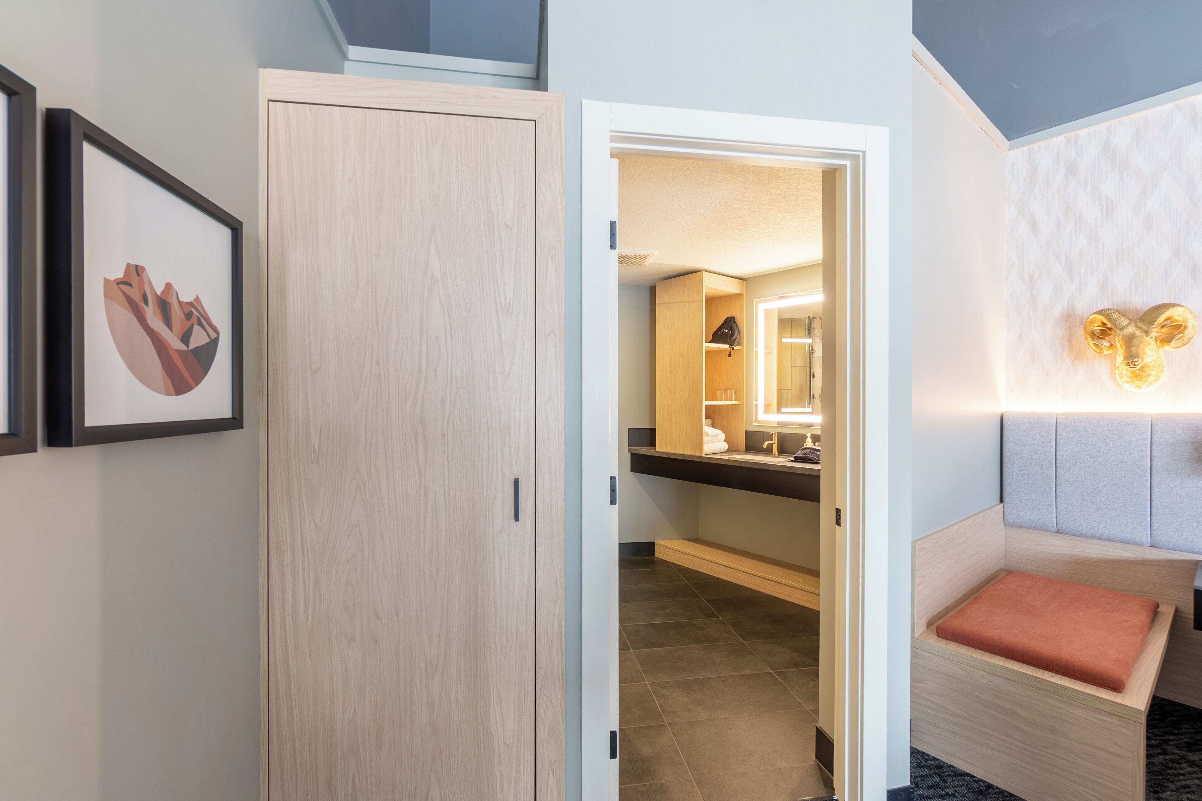 Hotelkamer met een houten garderobe, een ingelijst schilderij aan de muur, een badkamer met een spiegel en een decoratieve lamp.