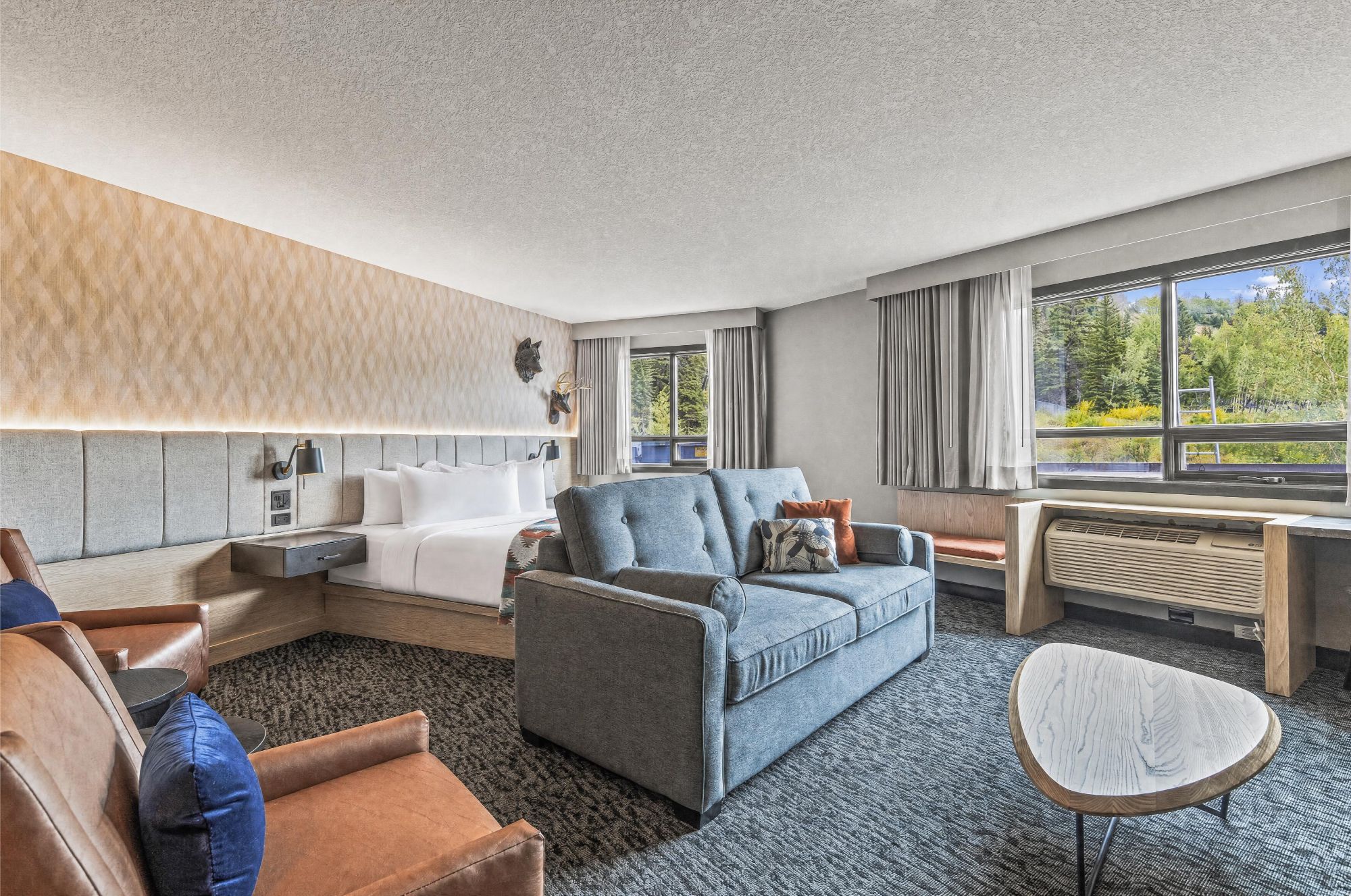 Habitación de hotel con sofá, una silla, una mesita, cama y ventana con vistas al verdor.