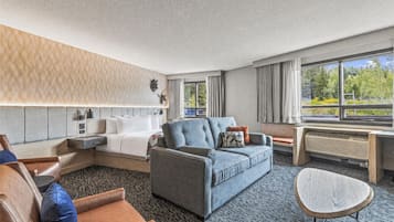 Habitación de hotel con sofá, una silla, una mesita, cama y ventana con vistas al verdor.