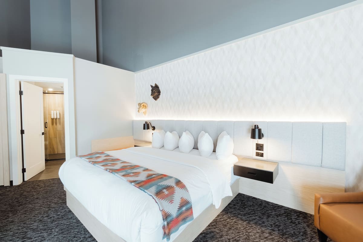Une chambre d’hôtel moderne avec un grand lit, une table de chevet, une lampe fixée au mur et une porte donnant accès à la salle de bain.