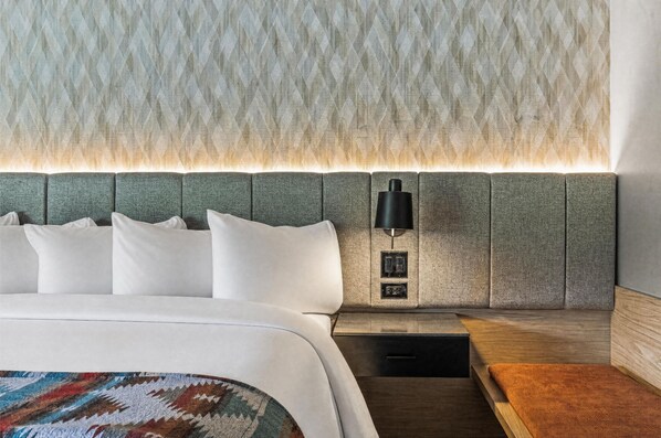 A modern hotel room with a large bed, a nightstand with a lamp, and a textured wall.