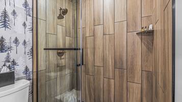 A shower with a glass door, wooden panel walls, and a shelf with toiletries.