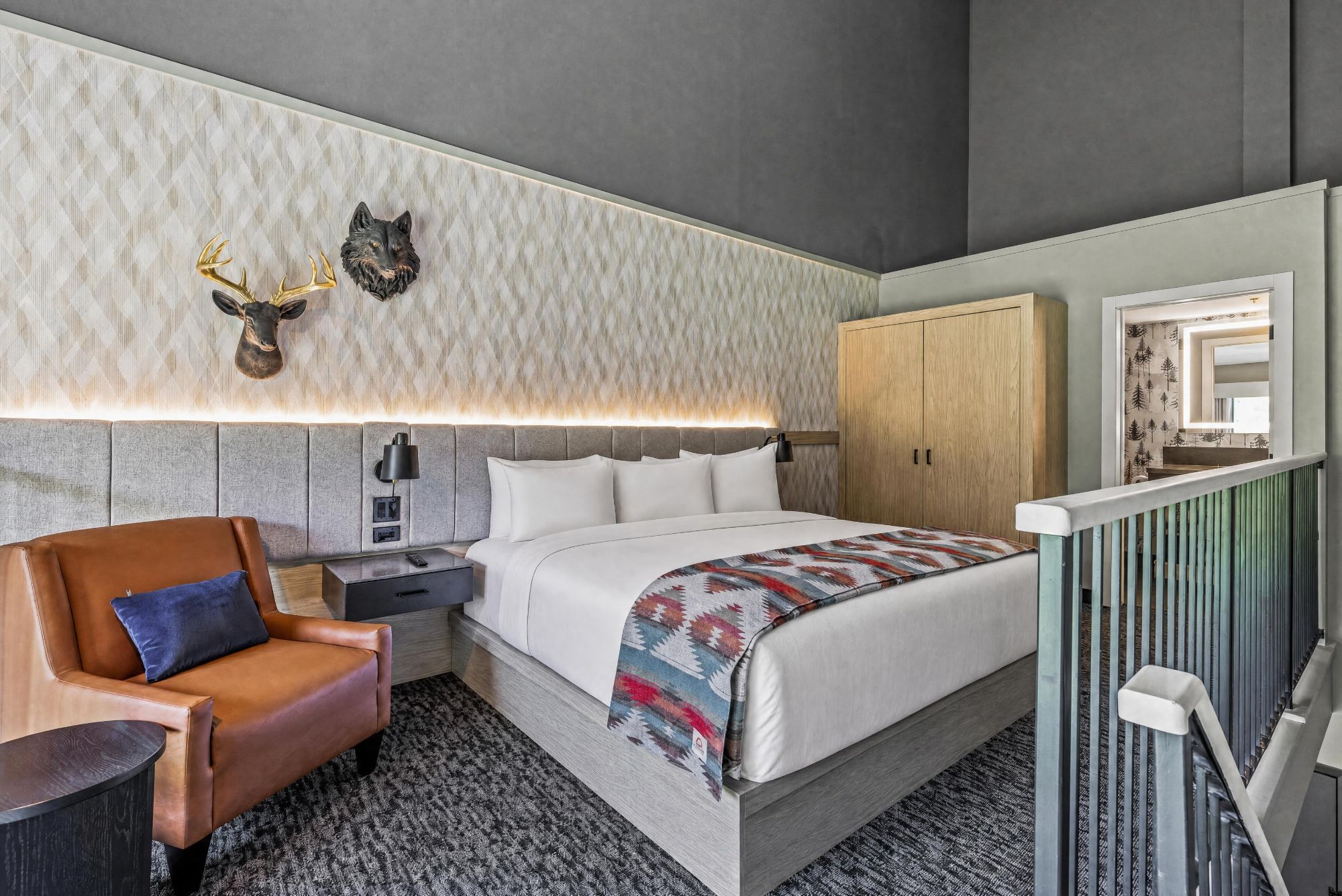 Una habitación de hotel con cama, mesita de noche, lámpara, silla, armario y espejo.