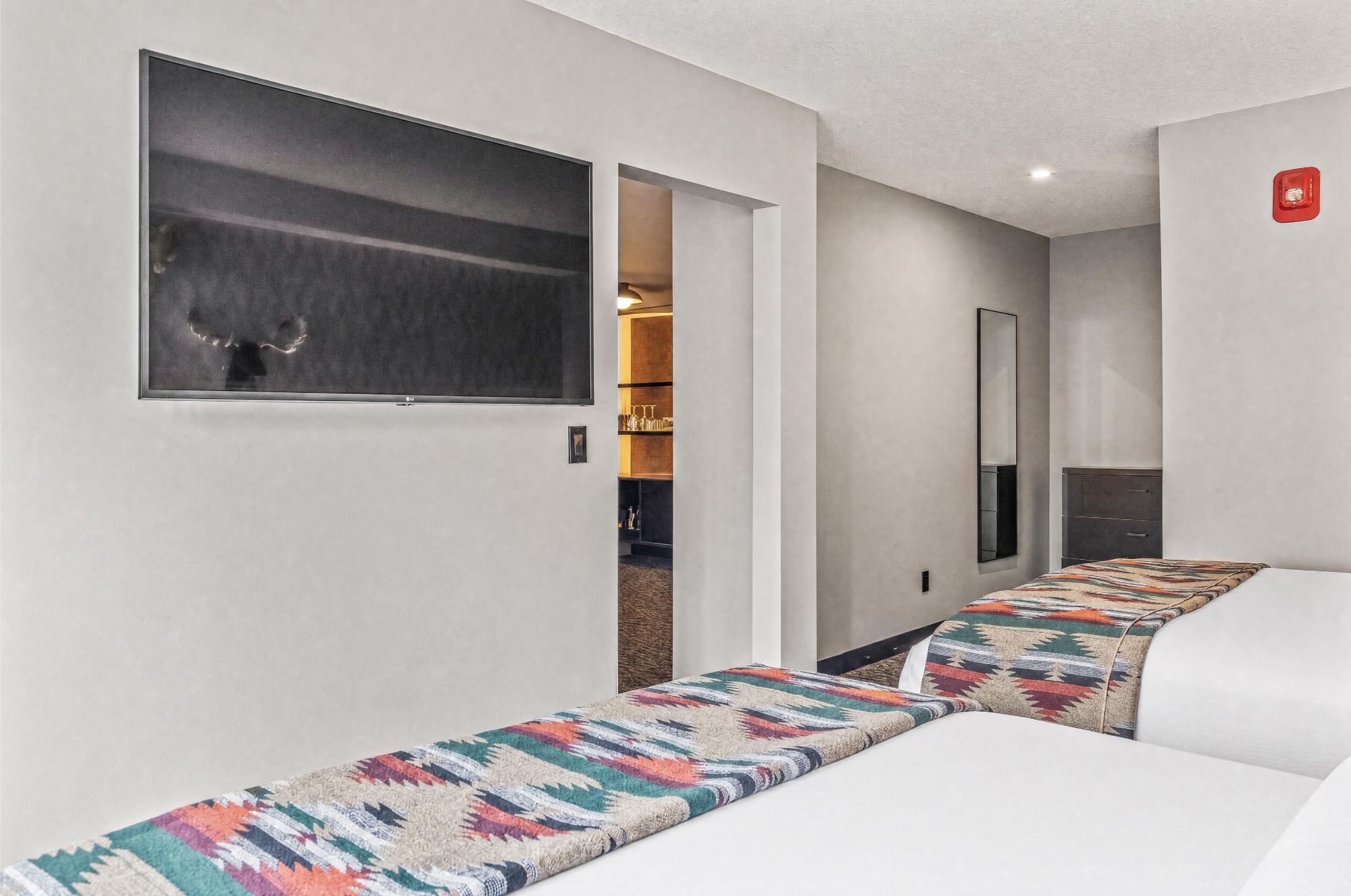 A hotel room with a bed, a large window, a mirror, and a door leading to a bathroom.