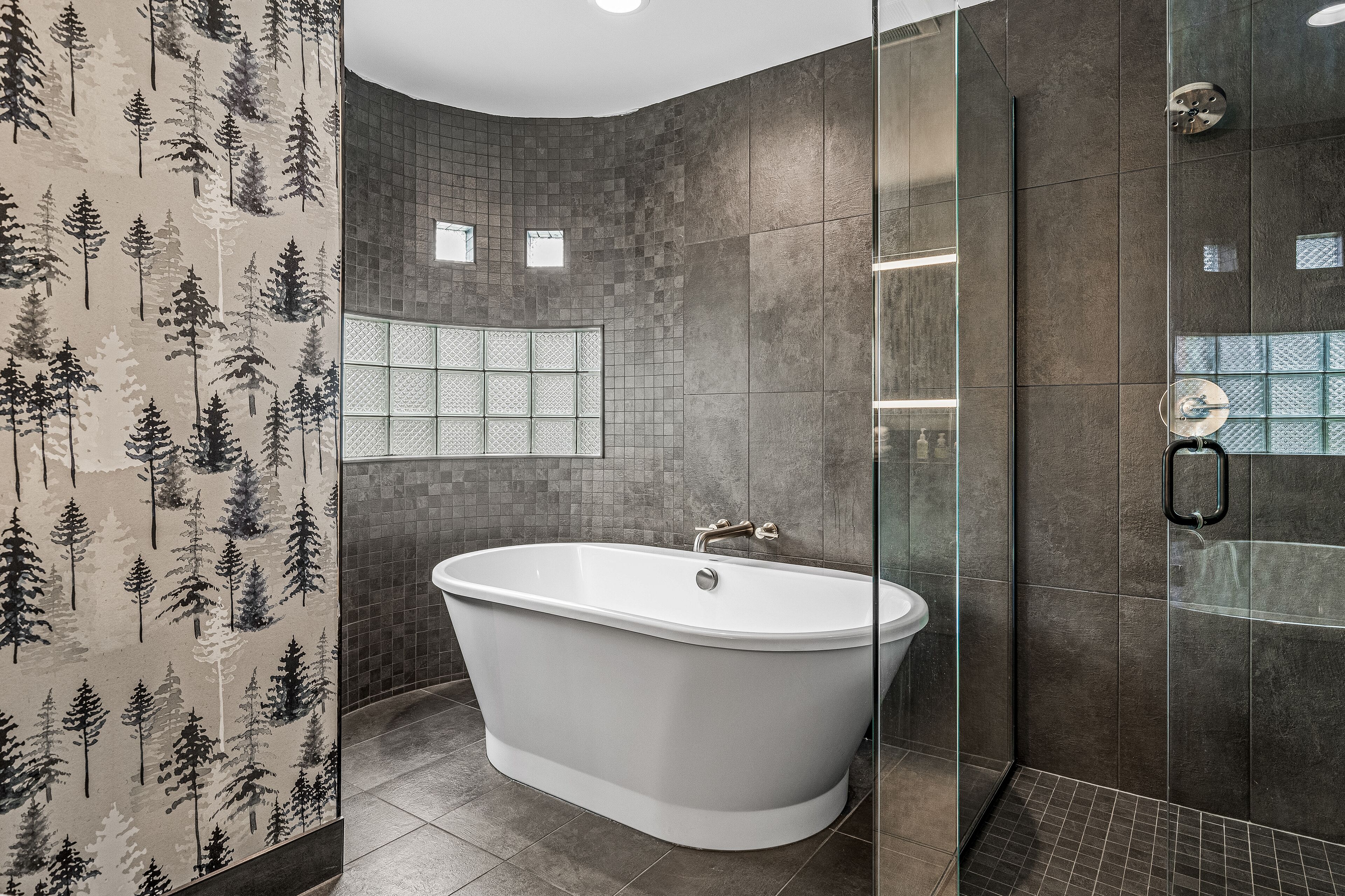 Un baño moderno con una bañera independiente, paredes con azulejos y una ventana con diseño de cuadrícula.