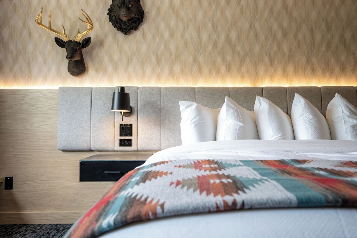 Une chambre d’hôtel moderne avec un grand lit, une tête de lit dotée d’un luminaire et une tête de cerf fixée au mur.