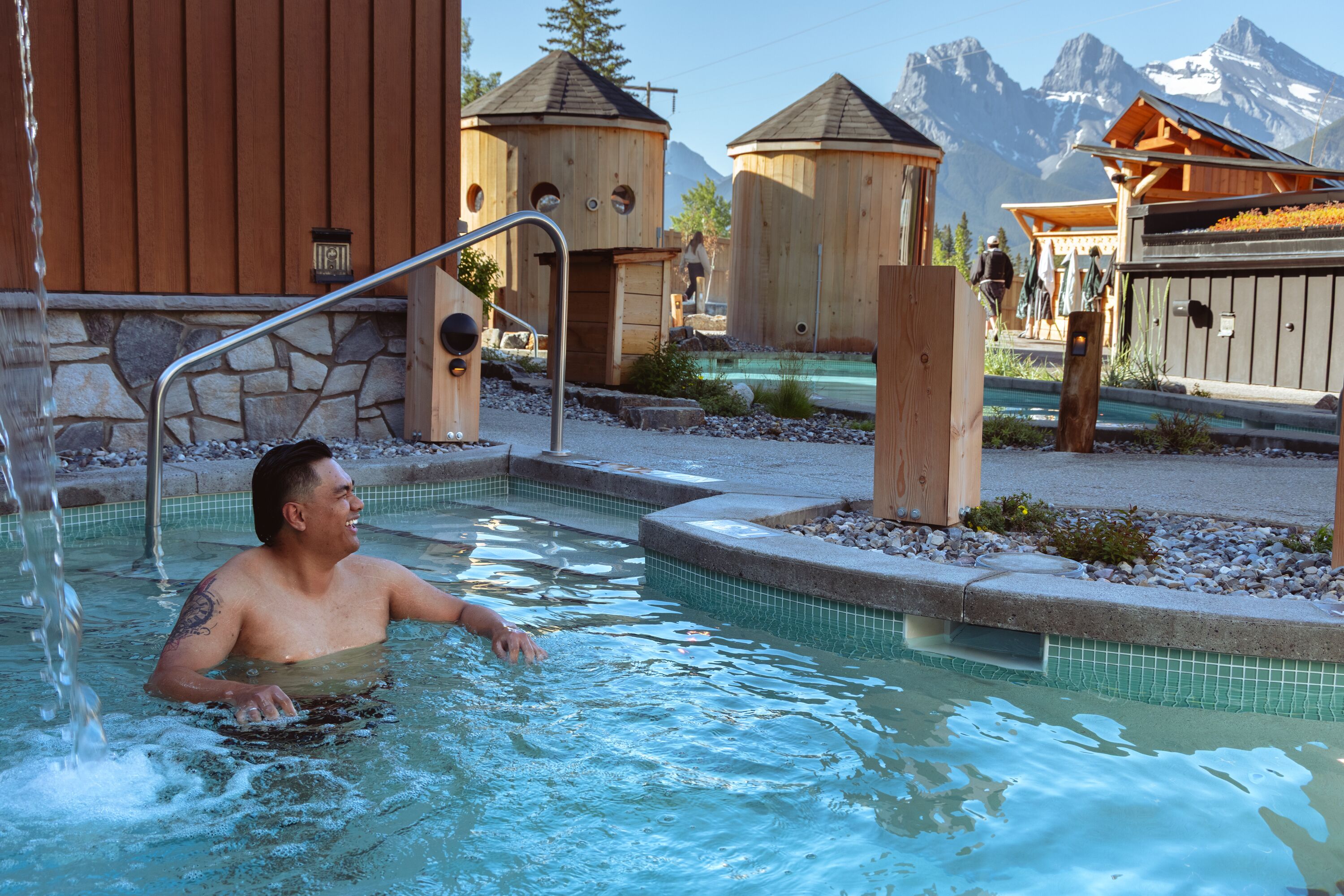 Un hombre en un jacuzzi con montañas al fondo.