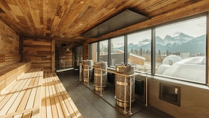 Un intérieur en bois avec un espace sauna, de grandes fenêtres offrant une vue sur les montagnes et un banc en bois.
