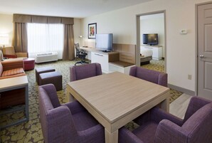 Une chambre d’hôtel avec une table à manger, des chaises violettes, un téléviseur, un bureau et un lit.