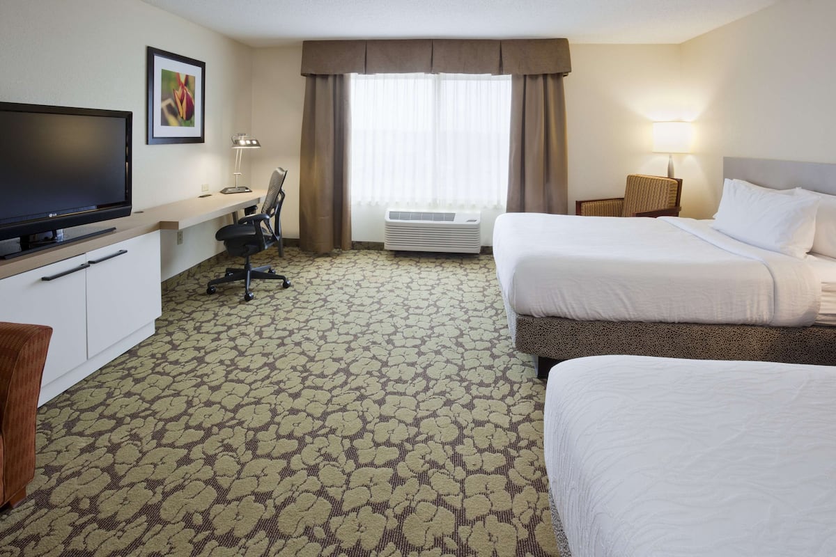 Quarto de hotel com duas camas, televisão, secretária, cadeira e ar condicionado.