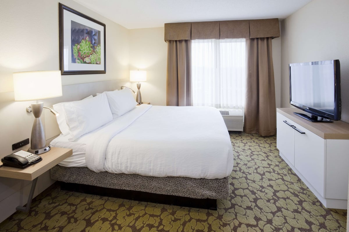 Quarto de hotel com uma cama grande, abajures, televisão e escrivaninha com telefone.
