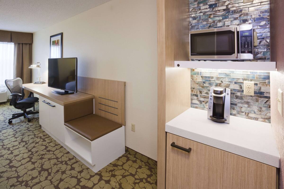 Quarto de hotel com cozinha compacta, televisão de tela plana, escrivaninha e cadeira.