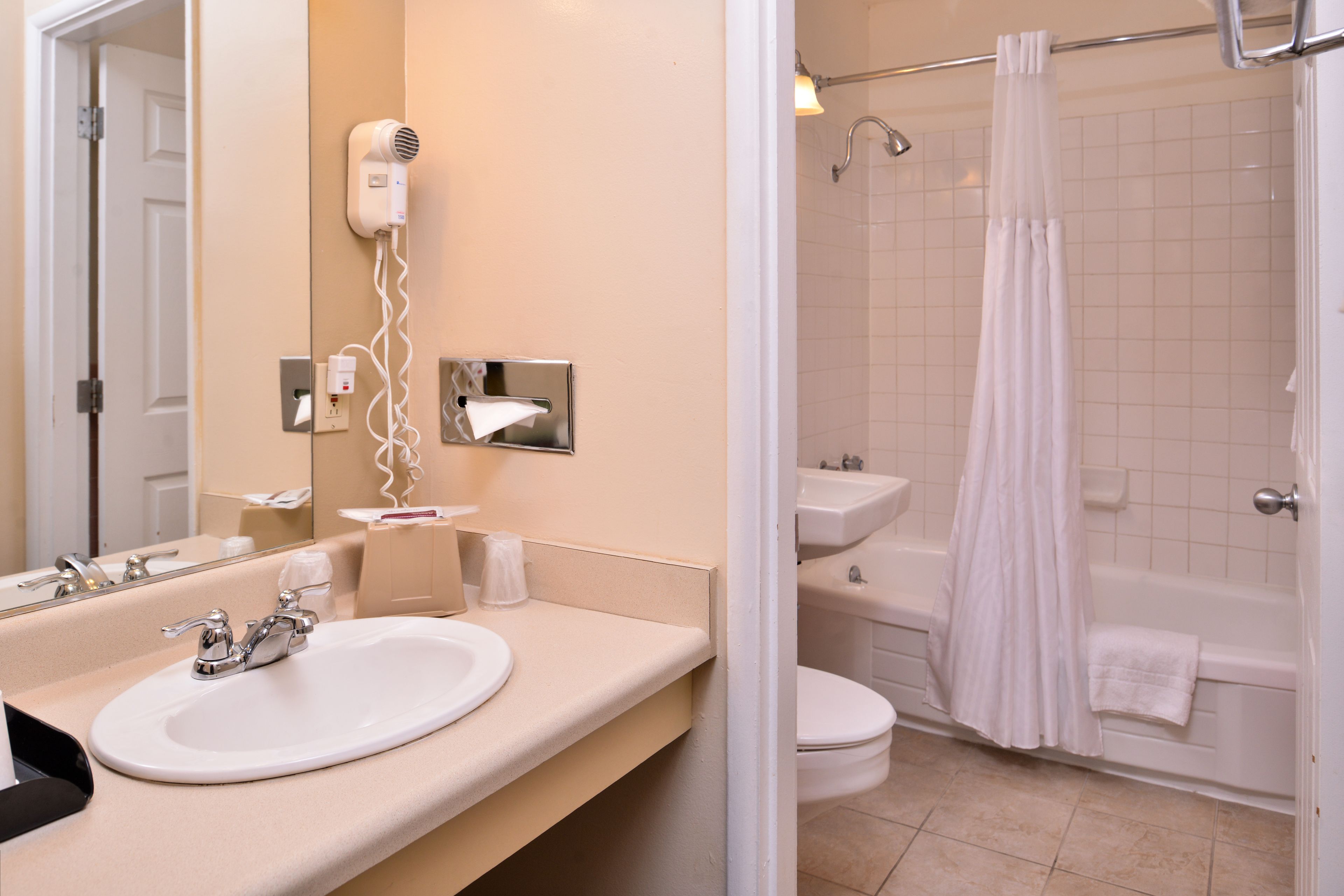 A bathroom with a sink, mirror, hair dryer, and a shower with a curtain.