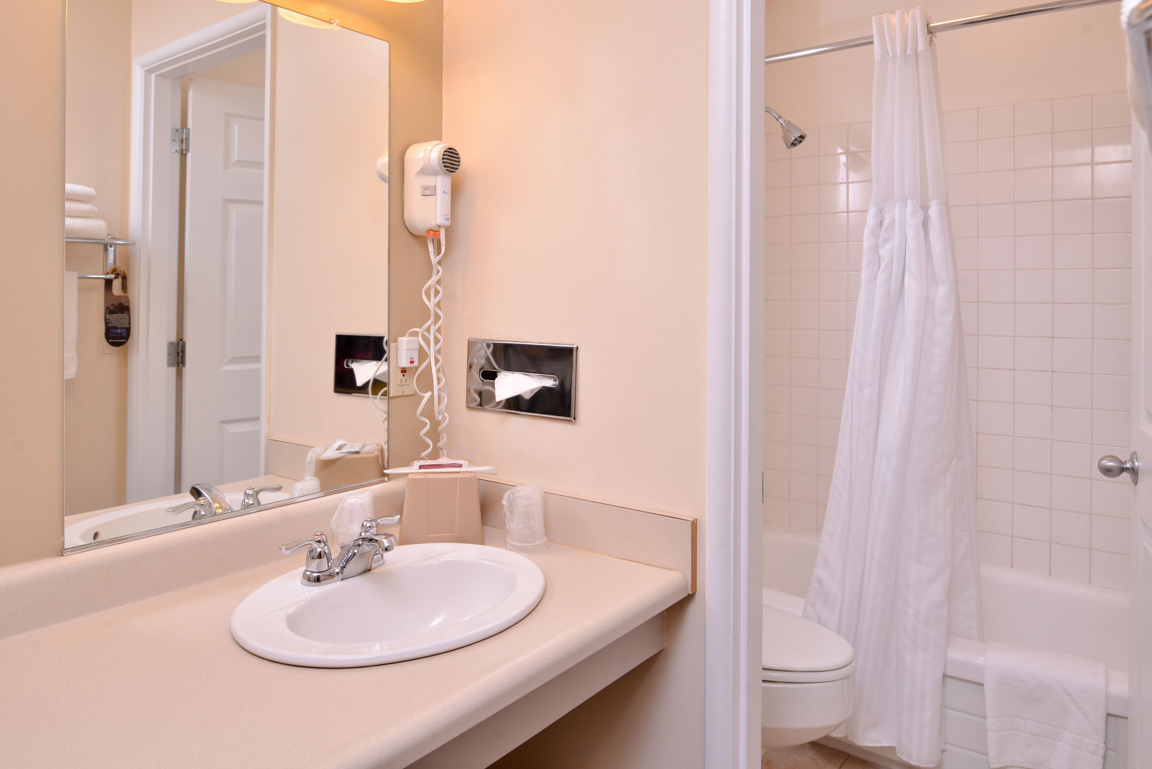 A bathroom with a sink, mirror, hairdryer, and a shower with a curtain.