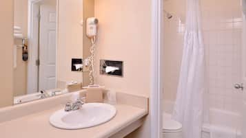 A bathroom with a sink, mirror, hairdryer, and a shower with a curtain.