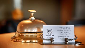 A hotel reception area with a silver bell and a business card displaying contact information and the hotel's address.