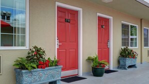 Un edificio con tres puertas rojas, numeradas 218, 219 y 220. Hay plantas en macetas frente a cada puerta.
