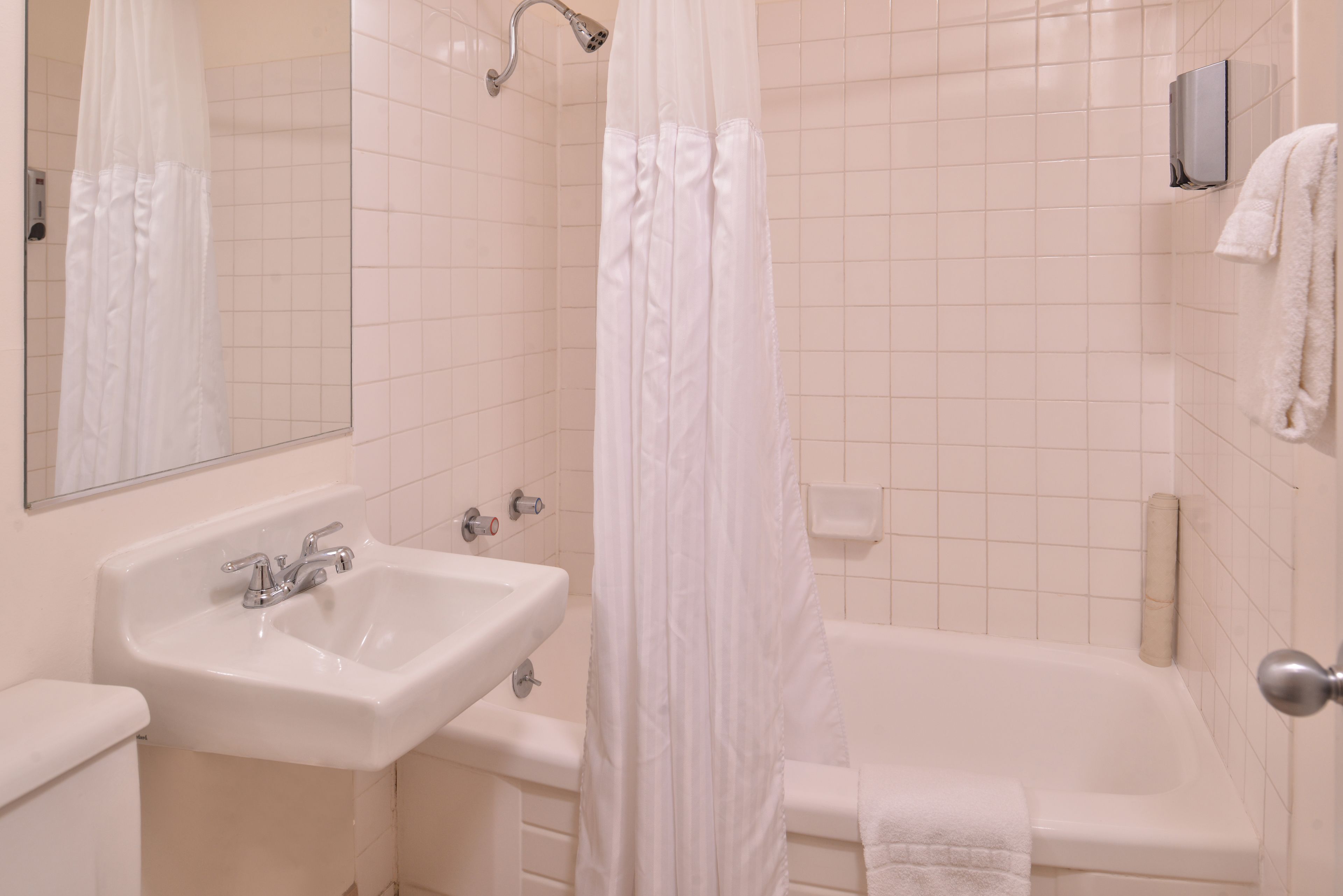 A bathroom with a sink, mirror, shower curtain, and a towel rack.