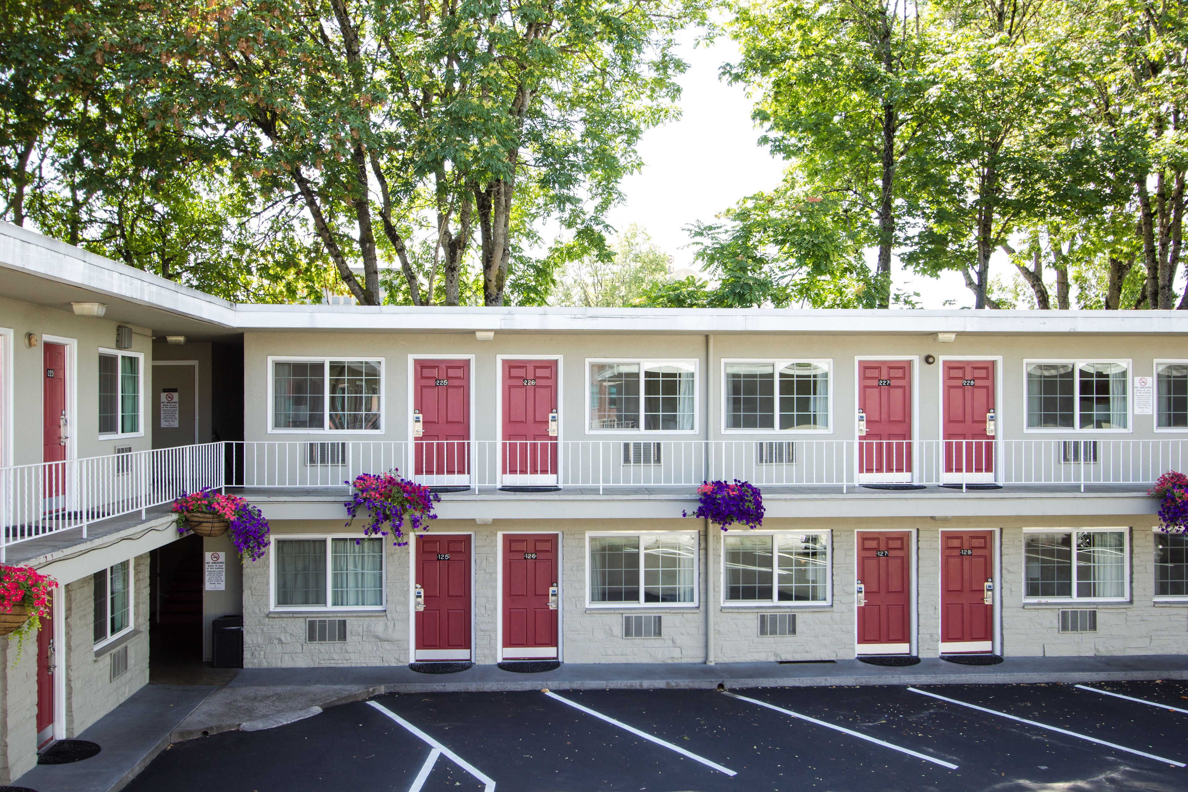 A two-story motel with red doors and windows, a covered parking area, and flower baskets on the balconies.