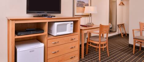 Quarto de hotel compacto com escrivaninha de madeira, televisão, micro-ondas, mini-geladeira, cadeira e espelho.