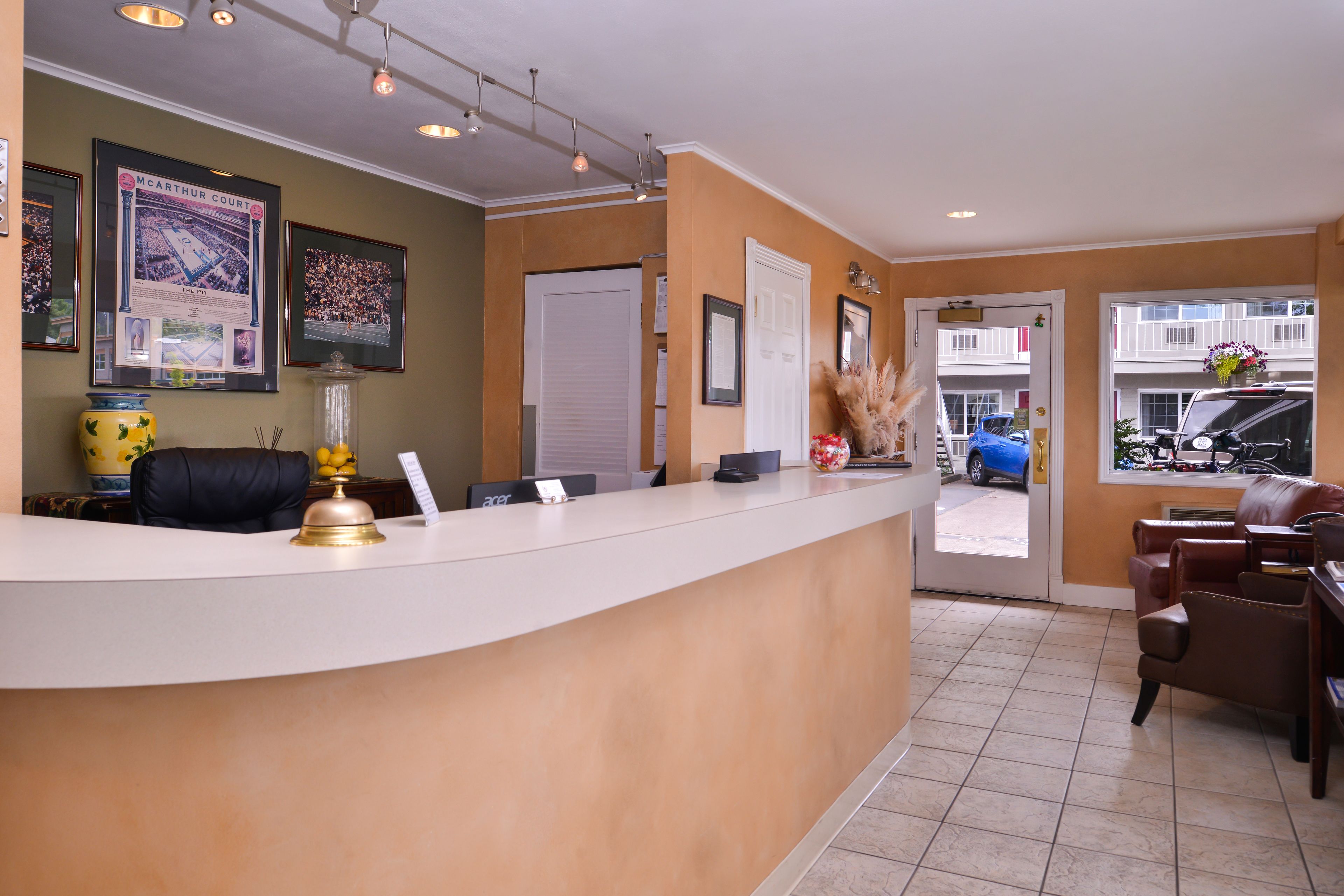 A reception area with a curved reception desk, framed pictures on the wall, a bell, and a vase with dried plants.