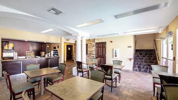 A restaurant with a bar area, multiple tables and chairs, a staircase, and a stone wall.