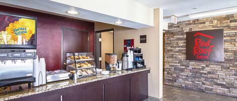 A Red Roof Inn breakfast area with a juice dispenser, pastries, and a coffee station.