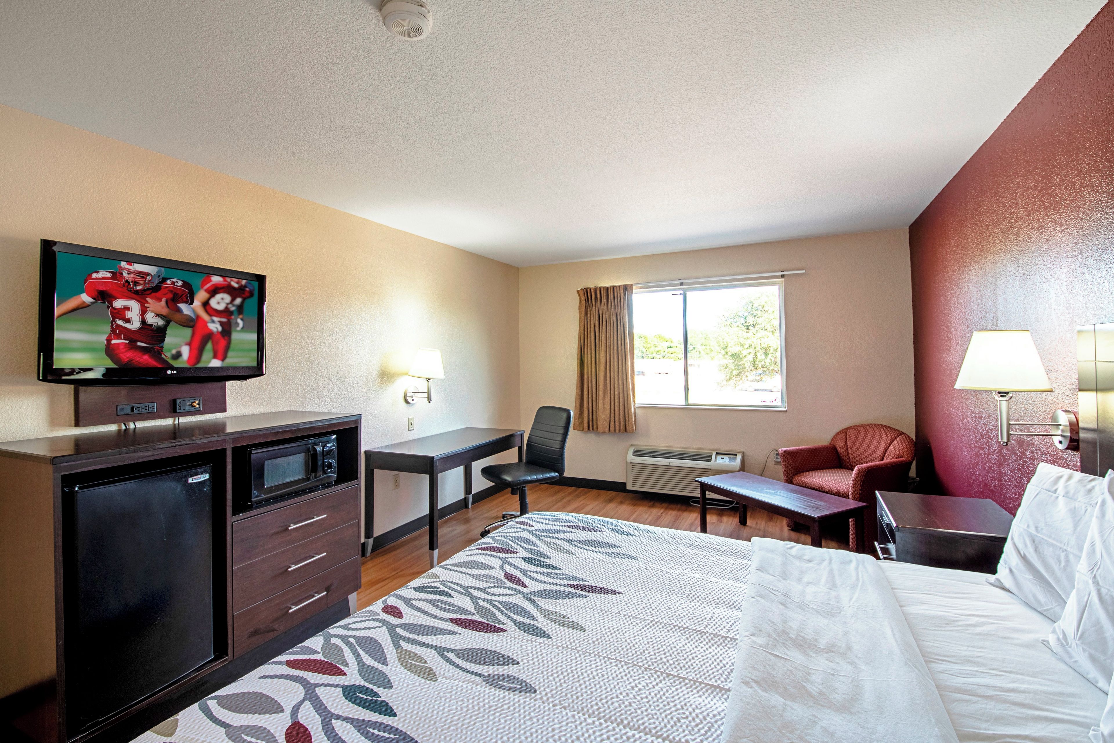 A hotel room with a bed, a desk, a television, a chair, and a window.