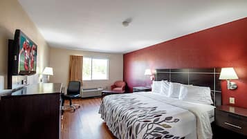 Una habitación de hotel con cama, escritorio, silla y televisor en la pared.