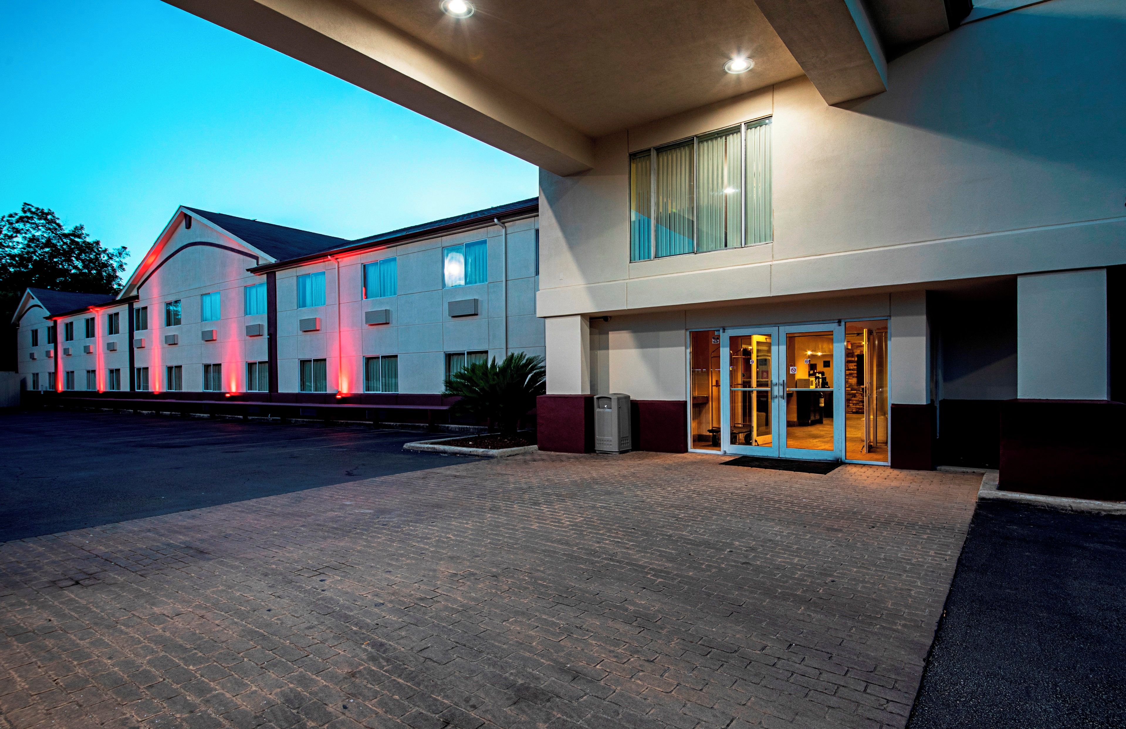 Un hotel con entrada empedrada en ladrillo, un corredor cubierto y un edificio con múltiples ventanales.