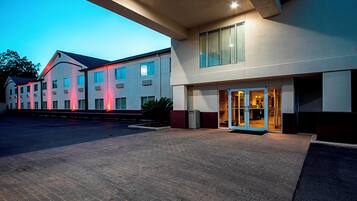 Un hotel con entrada empedrada en ladrillo, un corredor cubierto y un edificio con múltiples ventanales.