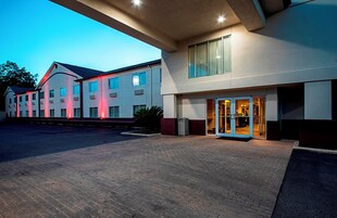 Un hotel con entrada empedrada en ladrillo, un corredor cubierto y un edificio con múltiples ventanales.