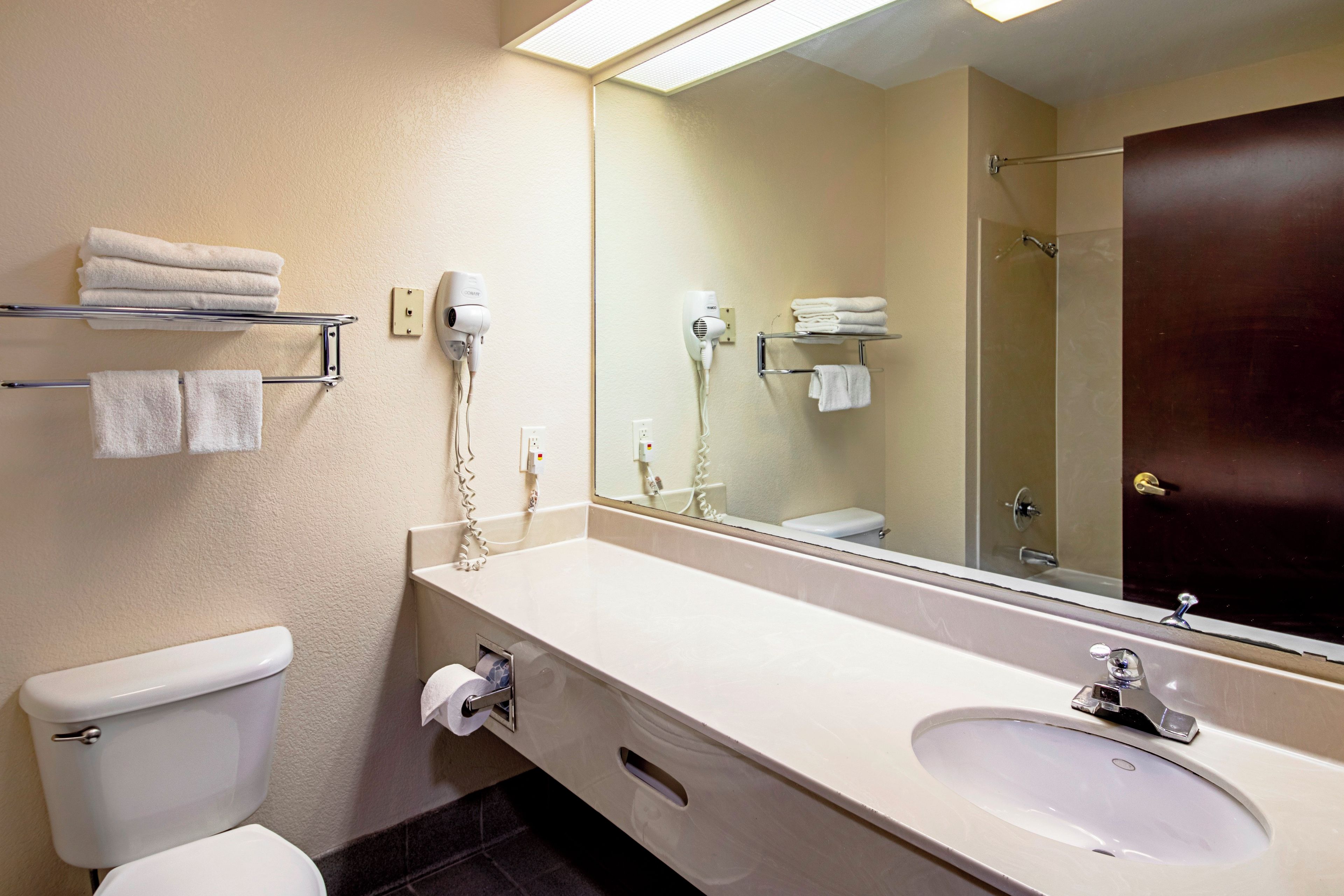 Un baño de hotel con inodoro, lavamanos, toallero y un espejo grande.