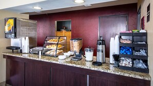 A breakfast bar with a coffee machine, a fruit display, and a beverage dispenser.