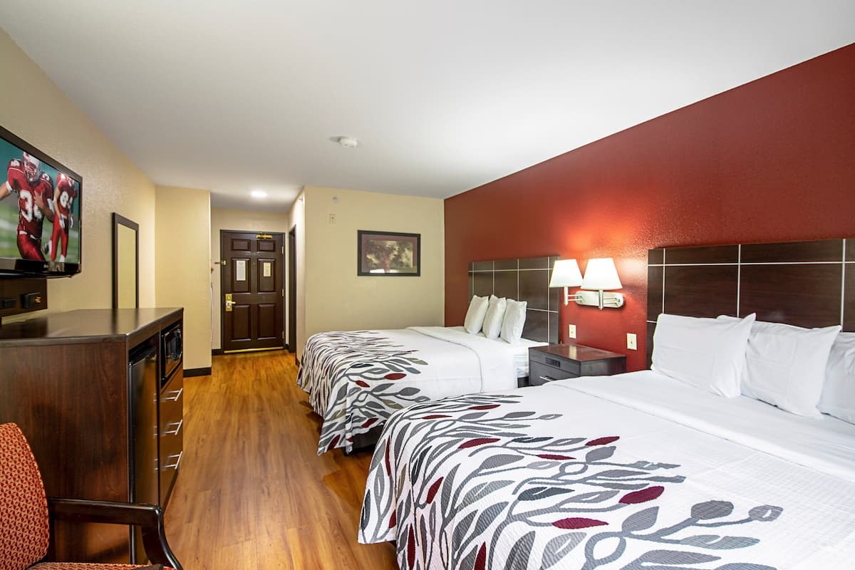 Une chambre d’hôtel avec deux lits, un bureau, une chaise, une télévision et une porte.