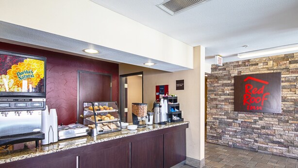 A breakfast bar with a coffee machine, juice dispensers, and pastries. There is a sign for Red Roof Inn and a stone wall.