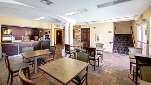 A restaurant with a counter, tables, and chairs. There is a staircase leading to another level.