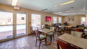 A hotel lobby with multiple tables and chairs, an exit sign, and a sign indicating free Wi-Fi availability.