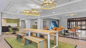 A modern indoor space with a long wooden table and benches, surrounded by chairs and a green carpet.