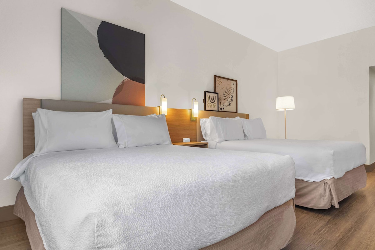 A hotel room with two beds, a large abstract painting, two wall-mounted lamps, and a floor lamp.
