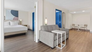 A modern hotel room with a bed, sofa, and a small table. There are two doors, one blue and one white, and a small table with chairs.