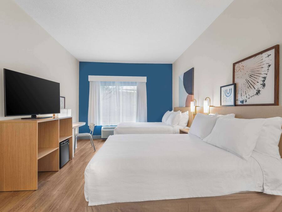 A hotel room with two beds, a TV, a desk, and a window with curtains.